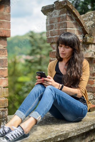 Woman using smartphone on ancient brick wall photo