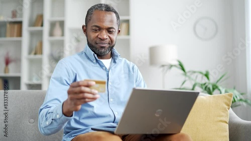 Wallpaper Mural Happy mature african american man doing online shopping typing credit card number on laptop sitting on sofa at home. Smiling senior bearded male makes purchase, satisfied with promotions and discounts Torontodigital.ca