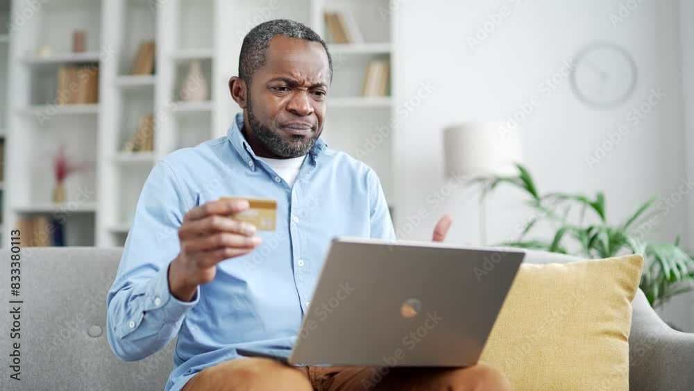 Frustrated mature african american man discovered fraud entering credit card number on laptop sitting in room at home. Upset senior male became a victim of deception, money was stolen from the account Frustrated mature african american man discovered fraud entering credit card number on laptop sitting in room at home. Upset senior male became a victim of deception, money was stolen from the account