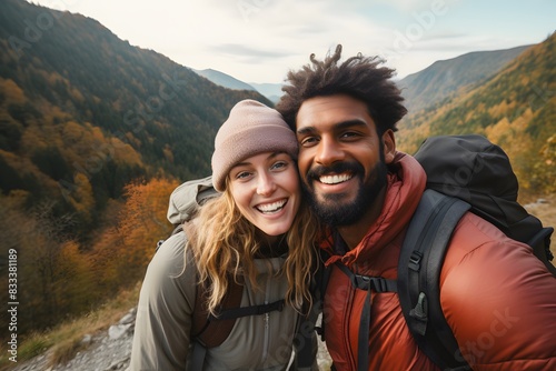 A happy couple hiking in a picturesque outdoor setting, dressed in warm clothing with backpacks, smiling at each other