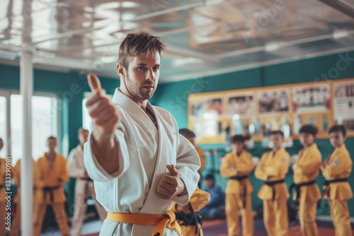 Martial arts instructor demonstrating technique to students in dojo. He is wearing white gi with yellow belt while students in yellow uniforms watch attentively photo