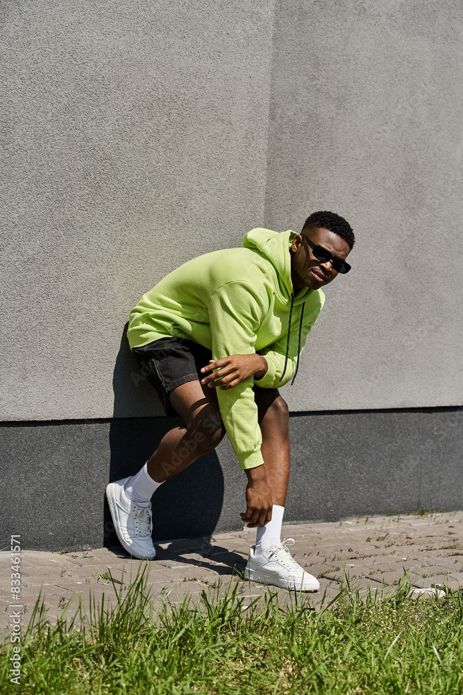 Stylish African American man in green hoodie leaning against a wall. Stylish African American man in green hoodie leaning against a wall.