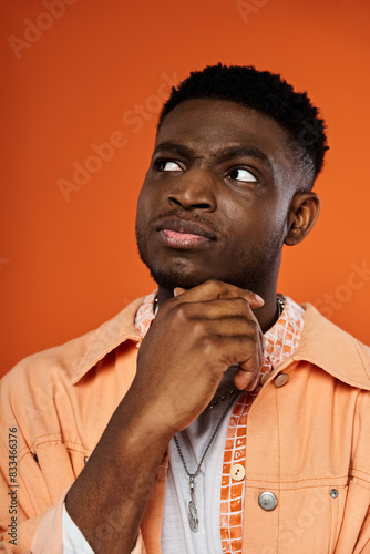 Fotografie Handsome African American man in orange shirt, chin resting on hand