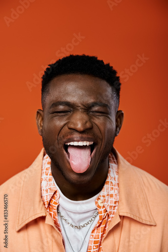 Handsome African American man playfully sticks out his tongue against a vibrant orange backdrop.