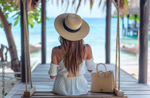 Travel summer vacation or holiday concept. Happy traveler young and beautiful woman with hat and dress relax on swing in beachside hotel or beach cafe photo