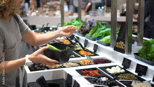 Woman selects ingredients for lunch at salad bar and puts them in her bowl. Quick lunch snack at supermarket with choice of fresh ingredients. Concept of choosing healthy foods for lunch.
