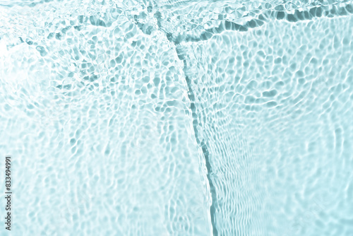 Close-up view of the surface of clear water formed by the interplay of light and ripples on water. Gentle waves create a mesmerizing texture  with circular ripples spreading out across the surface.