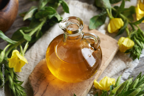 A glass bottle of evening primrose oil with fresh blooming plant