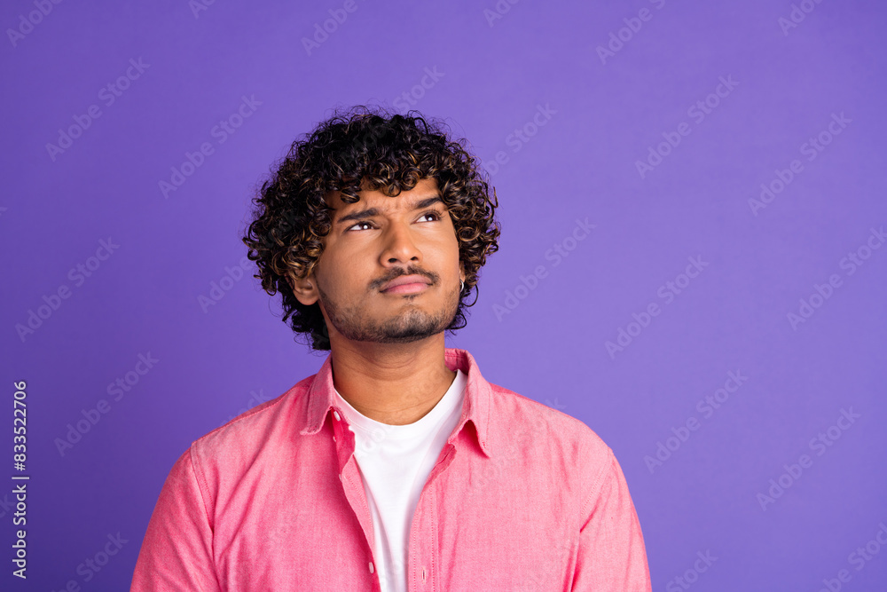Photo of nice young man look interested empty space wear pink shirt isolated on violet color background Photo of nice young man look interested empty space wear pink shirt isolated on violet color background
