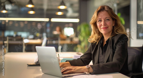 Friendly older woman smiling at camera, working on a laptop 