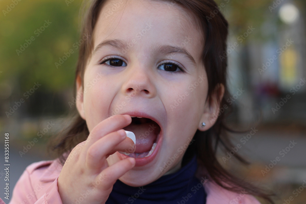 Childhood in Fall: Little Girl in Pink Raincoat and Blue Turtleneck Takes Medicine Childhood in Fall: Little Girl in Pink Raincoat and Blue Turtleneck Takes Medicine