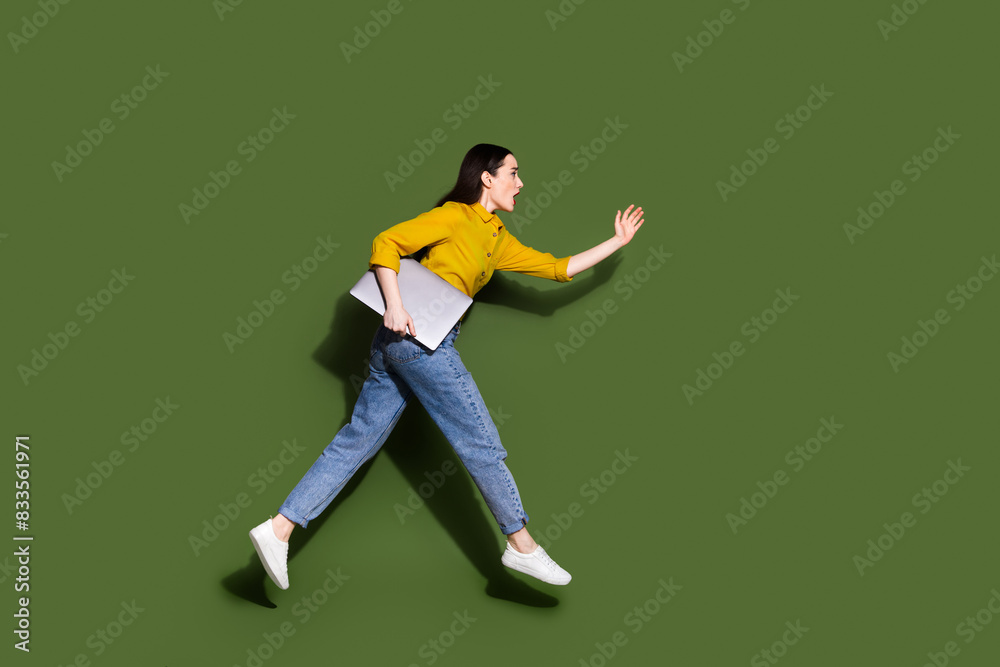 Full length photo of charming positive woman wear yellow shirt holding modern gadget jumping high isolated khaki color background Full length photo of charming positive woman wear yellow shirt holding modern gadget jumping high isolated khaki color background