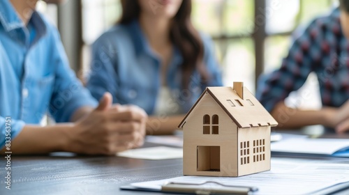 Model house on a table with people discussing in the background, symbolizing real estate investment and property planning.