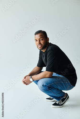 An African American man in a black shirt and jeans kneels down on a vibrant backdrop.