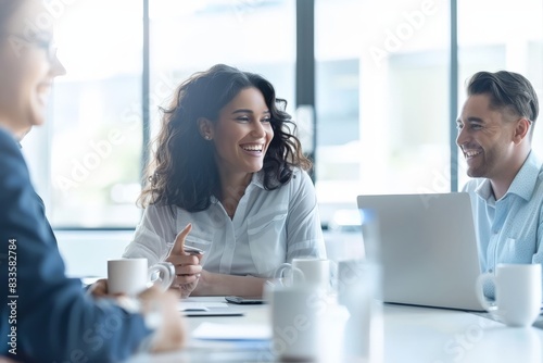 A group of professionals is seen having a lighthearted conversation at a coffee-laden table with a laptop