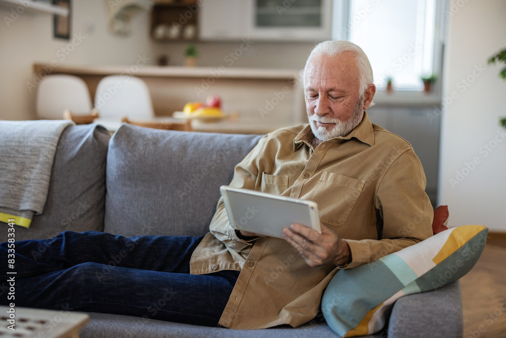 Smiling elderly businessman using digital tablet while sitting on couch at home. Smiling elderly businessman using digital tablet while sitting on couch at home.