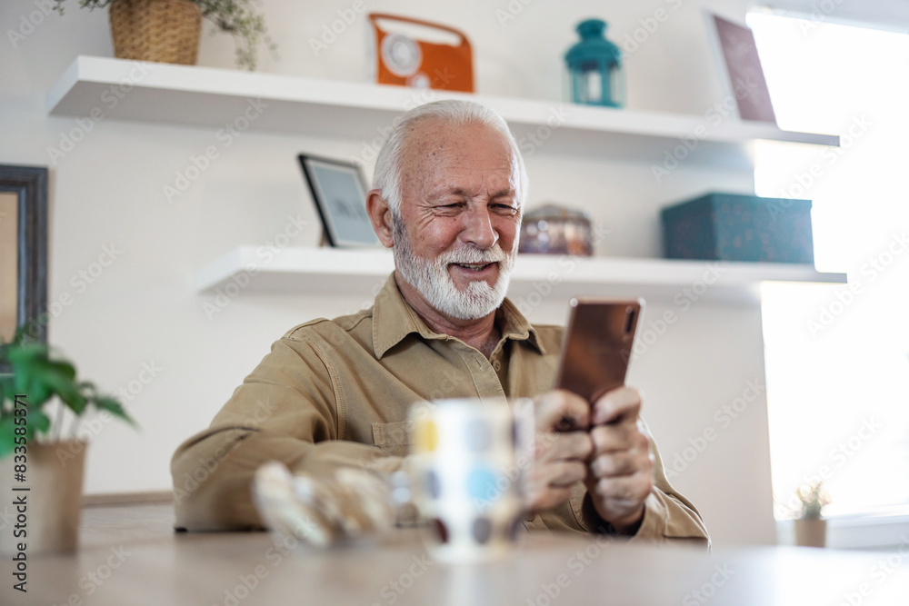 Senior man, morning coffee and phone looking happy while reading text message, online news or browsing internet in kitchen at home. Male using messenger or social media mobile app in his house. Senior man, morning coffee and phone looking happy while reading text message, online news or browsing internet in kitchen at home. Male using messenger or social media mobile app in his house.