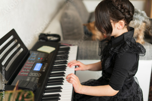 Cute little girl with glasses and a braid plays the piano in a black dress