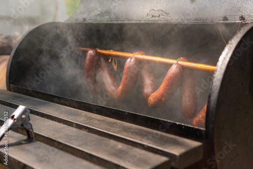 Foto Smoked sausages hanging on rack in a offset smoker with a thick smoke, closed up