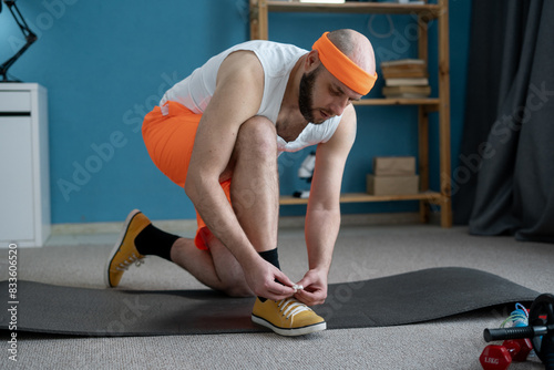 Man prepares for home workout on yoga mat in home gym, tying sneakers for indoor exercise photo