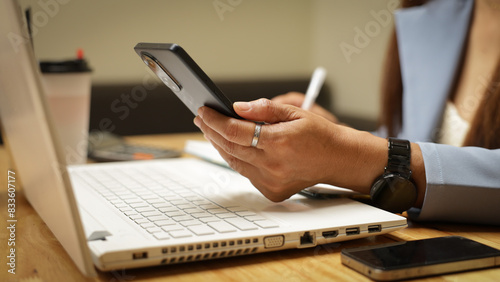 Fotografie A woman is sitting at a desk with a laptop and a cell phone