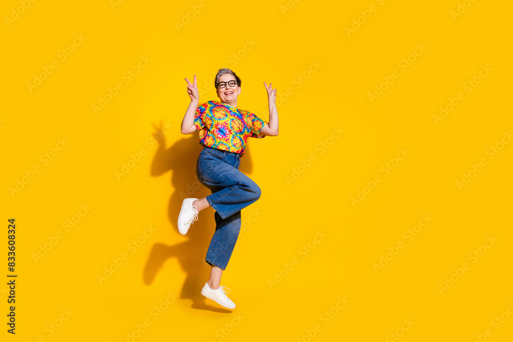 Full body portrait of nice aged lady jump show v-sign wear t-shirt isolated on yellow color background Full body portrait of nice aged lady jump show v-sign wear t-shirt isolated on yellow color background