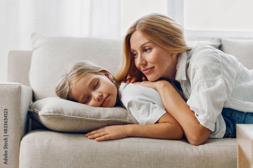 Mother and daughter relaxing on a white couch, enjoying quality time together in a cozy living room setting Mother and daughter relaxing on a white couch, enjoying quality time together in a cozy living room setting