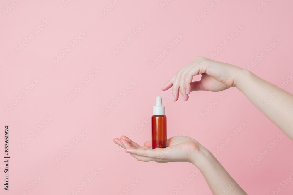 Fototapeta premium Hand holds serum glass brown bottle (essential oil) with pipette. Luxury product cosmetic advertising