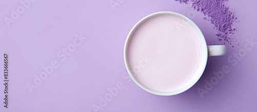 A white cup containing lavender moon milk is seen from a top view on a violet surface The image has copy space available