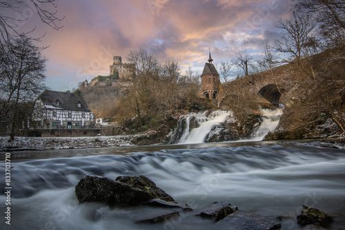 Beautiful landscape in winter with ice and snow. Waterfall of the River Elz near Pyrmont Castle, the Pyrmonter Mühle country inn is right on a lake. A historical bridge in Rhineland Pflaz, Germany photo