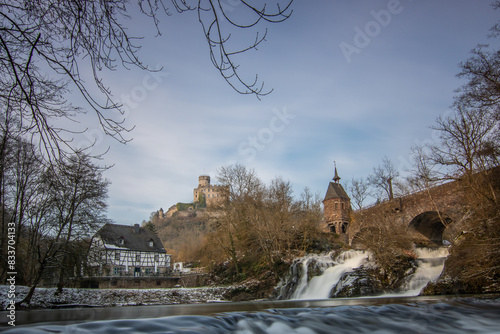 Beautiful landscape in winter with ice and snow. Waterfall of the River Elz near Pyrmont Castle, the Pyrmonter Mühle country inn is right on a lake. A historical bridge in Rhineland Pflaz, Germany photo