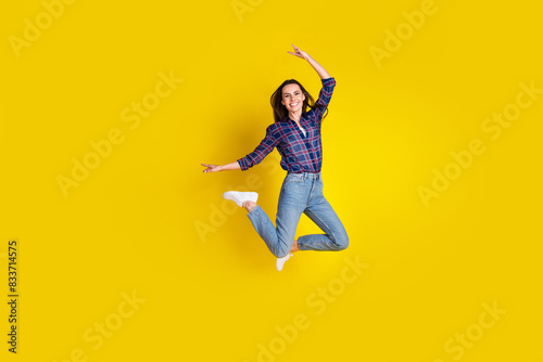 Full length photo of lovely young lady jump have fun dressed stylish plaid garment isolated on yellow color background photo