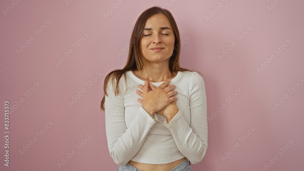 Obraz premium Young caucasian woman in a white shirt standing over an isolated pink background with her hands on her heart, evoking a serene and heartfelt emotion.
