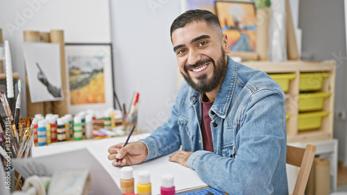 Konstfotografi A smiling young man with a beard painting in an art studio, giving a look of creativity and enjoyment