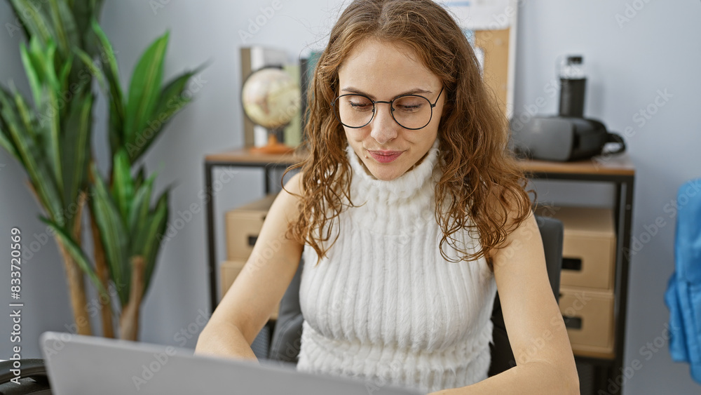 A young woman works attentively at her laptop in a modern office, exuding professionalism and focus. A young woman works attentively at her laptop in a modern office, exuding professionalism and focus.