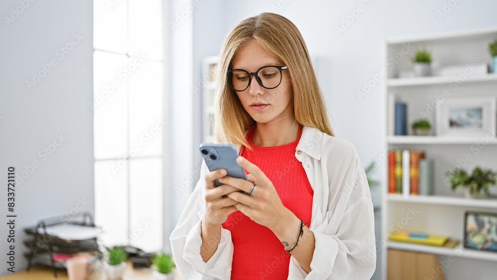 A focused young woman using her smartphone in a modern office setting. A focused young woman using her smartphone in a modern office setting.