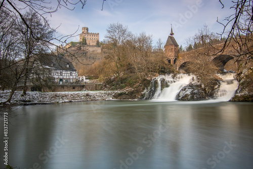 Beautiful landscape in winter with ice and snow. Waterfall of the River Elz near Pyrmont Castle, the Pyrmonter Mühle country inn is right on a lake. A historical bridge in Rhineland Pflaz, Germany photo