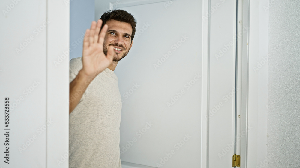 Smiling young hispanic man with a beard waving hello indoors, evoking a friendly greeting at home. Smiling young hispanic man with a beard waving hello indoors, evoking a friendly greeting at home.