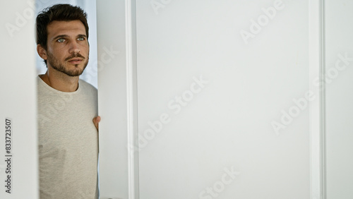 Fotografie Handsome hispanic man with beard standing thoughtfully in a minimalist interior room, evoking modern home lifestyle