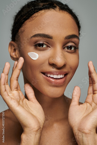 Young African American woman applying cream to her face, focused on skincare routine, exuding confidence and beauty.