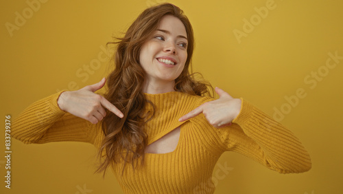 Beautiful young blonde woman in a yellow sweater smiling and pointing at her chest over an isolated yellow background.