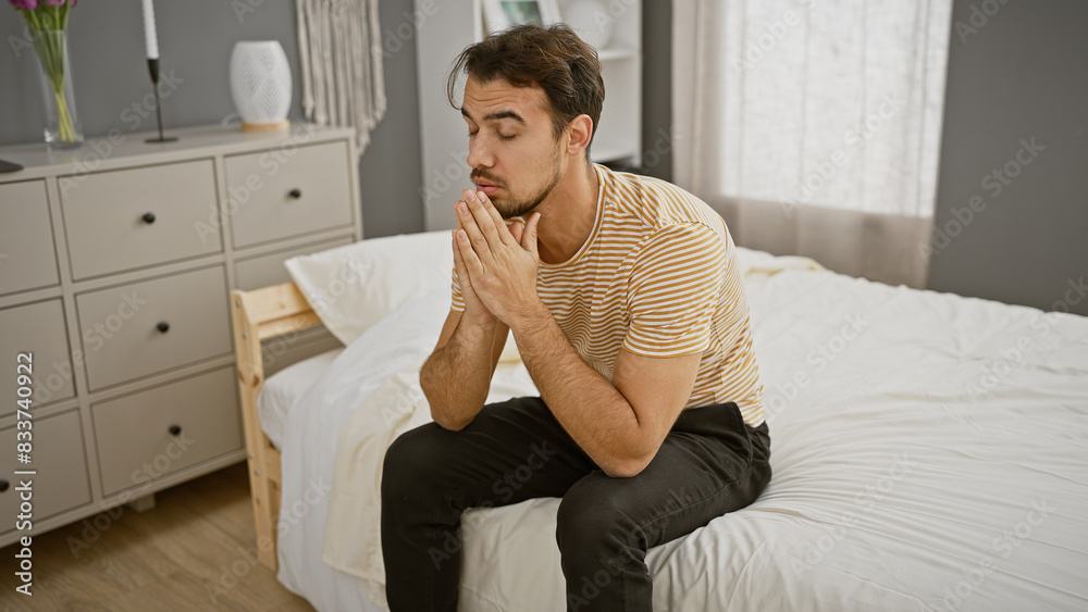 Handsome pensive hispanic man with beard sitting on bed in modern bedroom contemplating Handsome pensive hispanic man with beard sitting on bed in modern bedroom contemplating