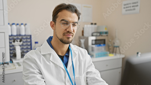 Handsome young hispanic man with beard wearing glasses and lab coat in a scientific laboratory setting