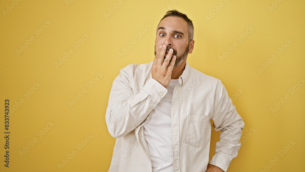Surprised mature hispanic man with grey beard against a yellow background.