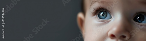 Close-up of a baby's blue eyes gazing upwards with a soft focus on a dark background, capturing innocence and curiosity.