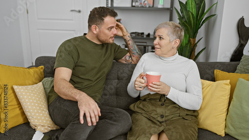 A man and woman sitting close on a couch, exchanging glances in a cozy living room, evoking a sense of intimacy and casual comfort.