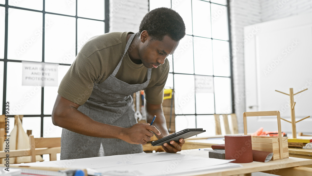 African american man focusing on a tablet while working in a bright carpentry workshop