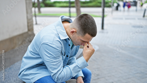 Thoughtful young hispanic man sitting outdoors on a city street, posing for a lifestyle portrait. © Krakenimages.com