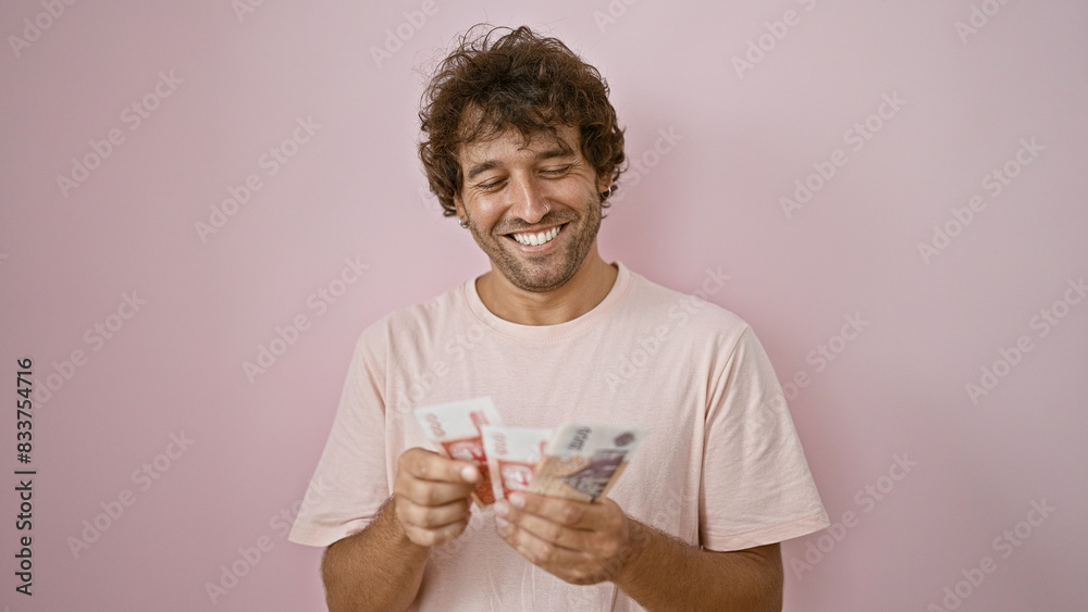 Handsome young man smiling while holding icelandic kronur against a pink background Handsome young man smiling while holding icelandic kronur against a pink background