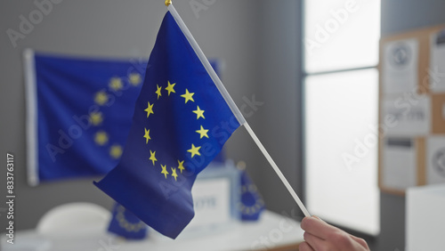 Young man holds a european union flag in a room with ballot boxes, symbolizing democracy and voting in europe.